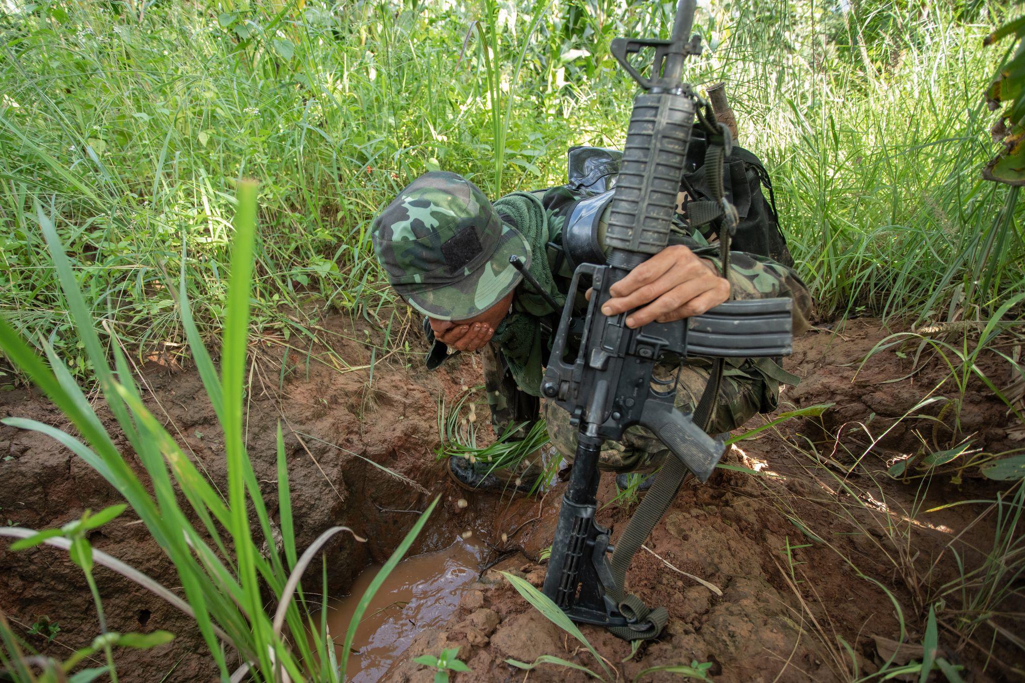 A soldier holding a gun crouching in the grass with his face obscured by his helmet